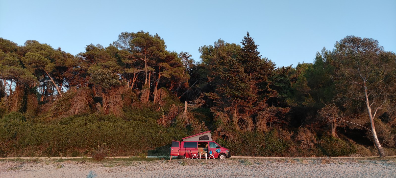 Red camper on a beach beside a forest in the evening light