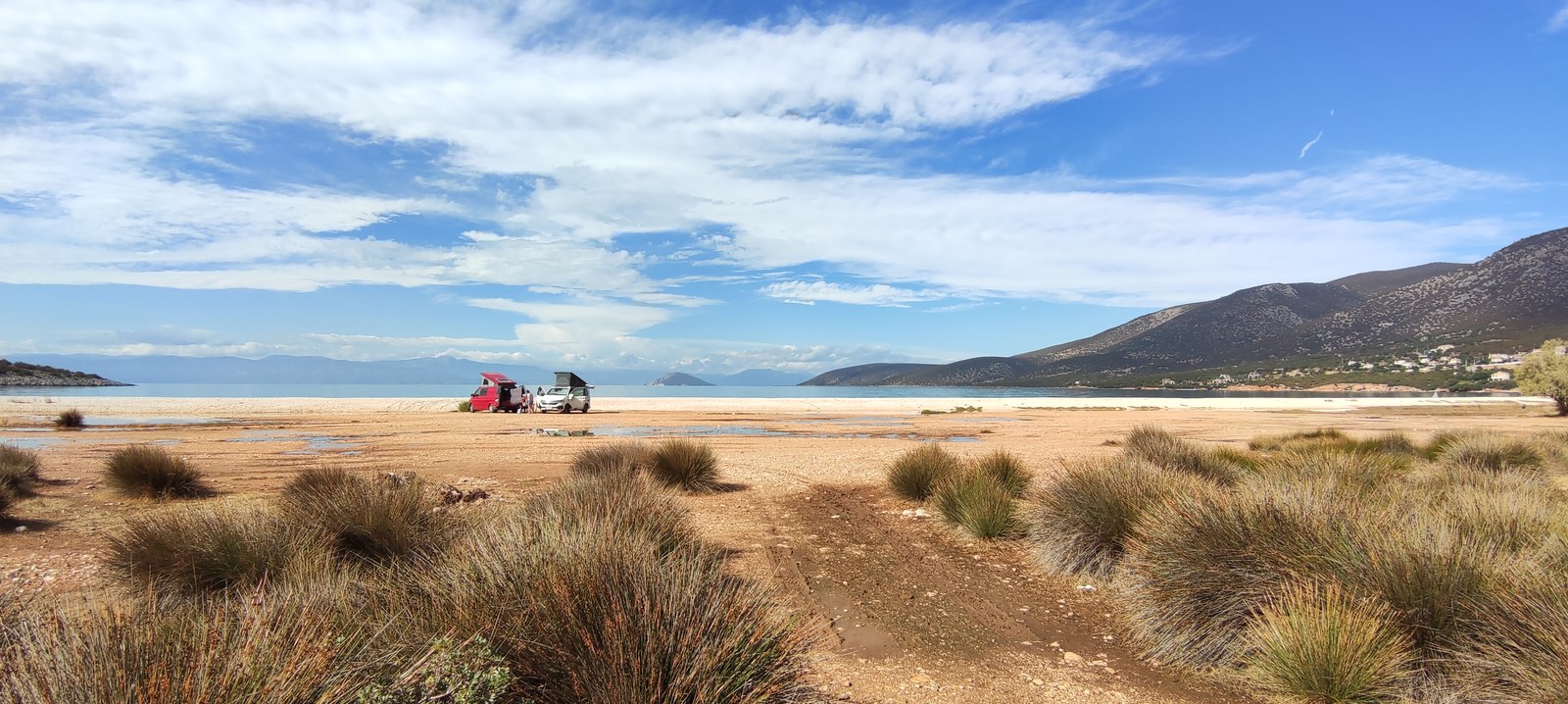 Two campers on a wide beach with mountains in the background