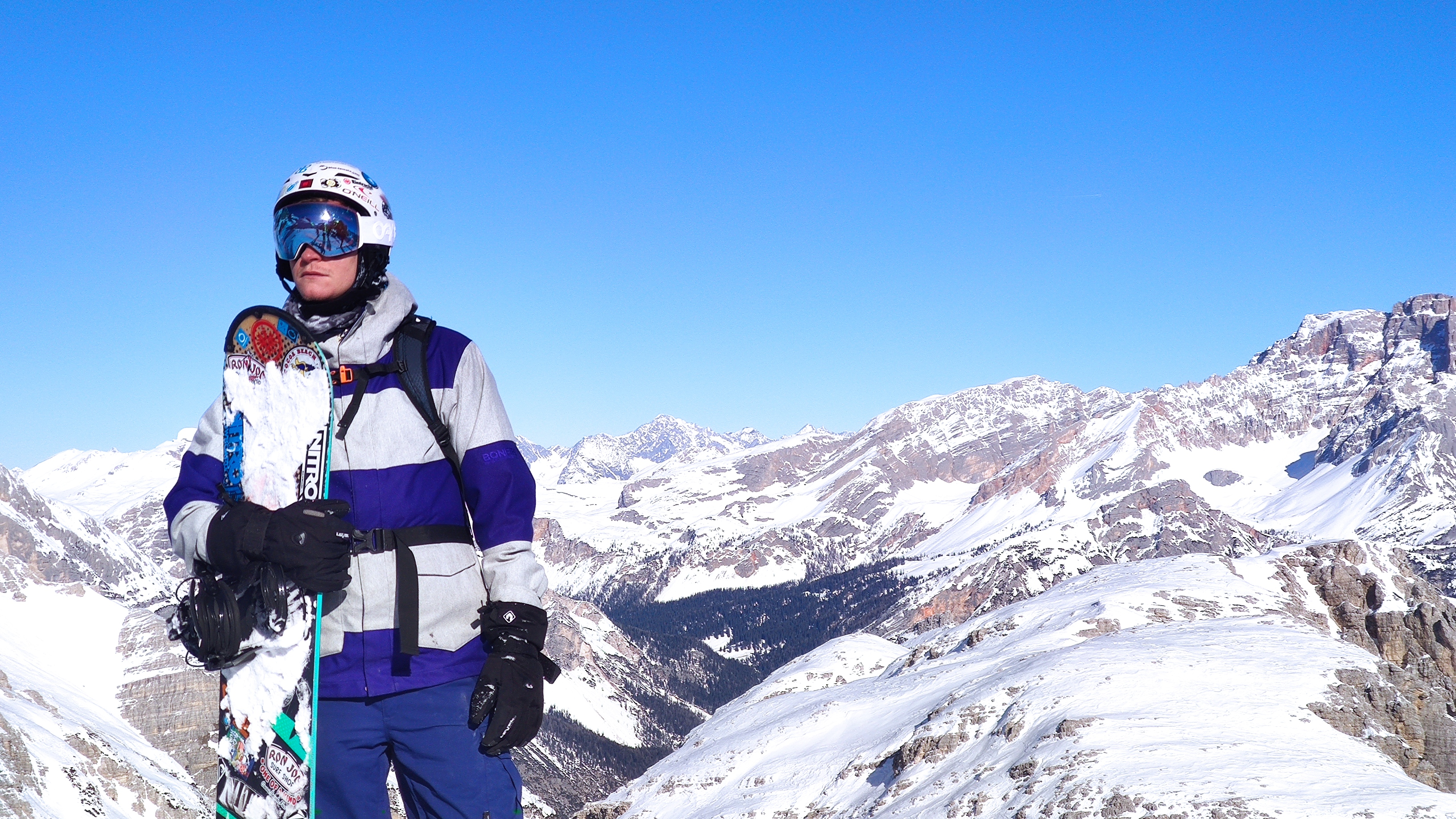 Snowboarder in front of snow-covered mountains under a blue sky